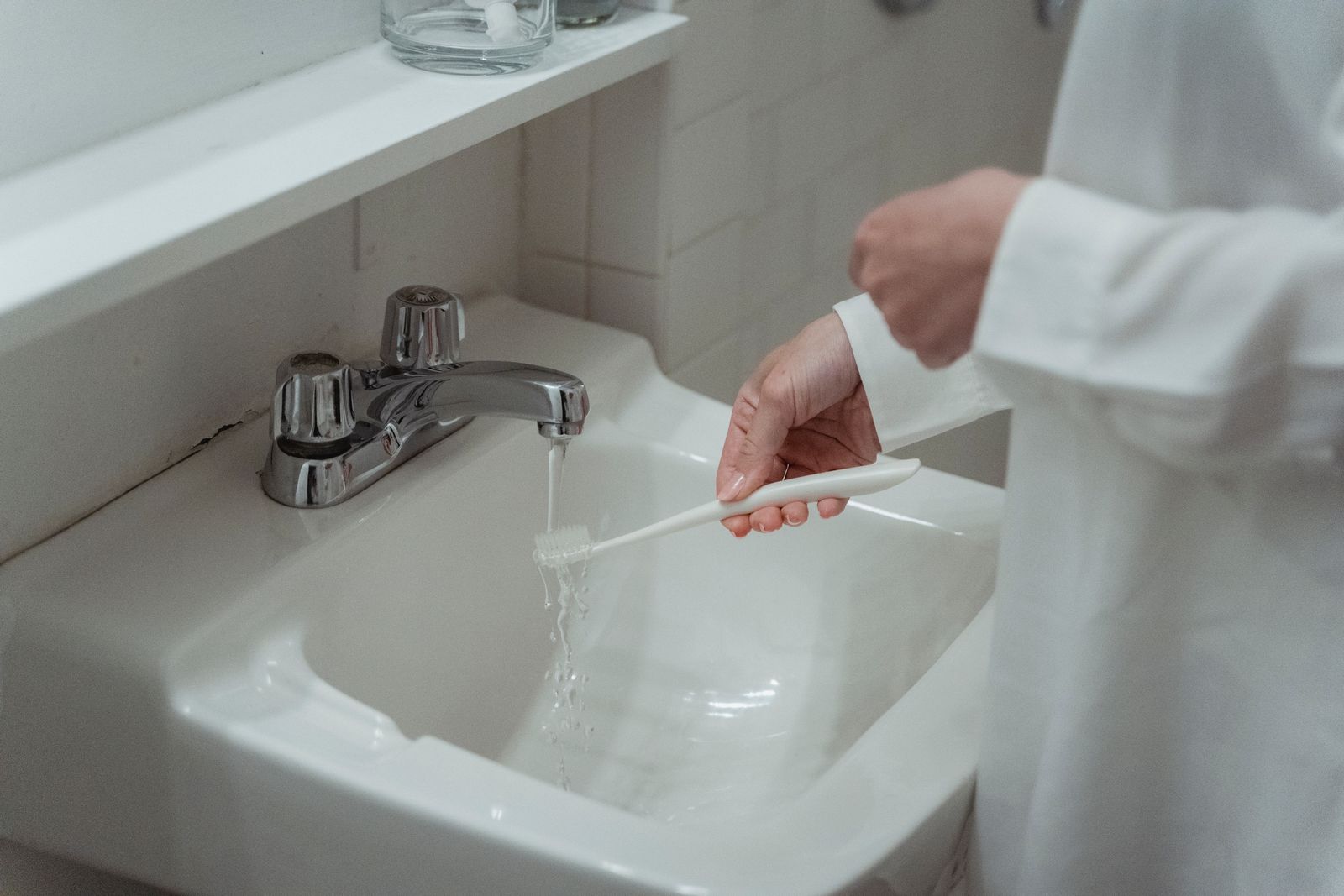 A toothbrush being rinsed over a white bathroom sink